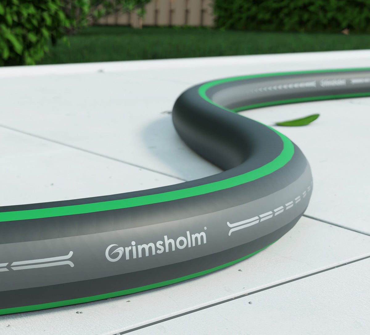 Grimsholm Classic Haveslange 10 m, sort og grå med grøn stribe, fleksibel vandslange nær grønne planter.