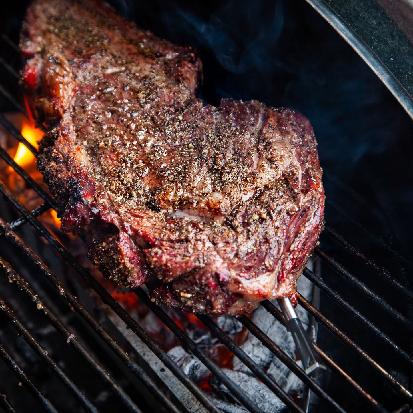 Meater+ trådløs grilltermometer og repeater overvåger temperatur ved bøf på grill, røg ses ved stegen.