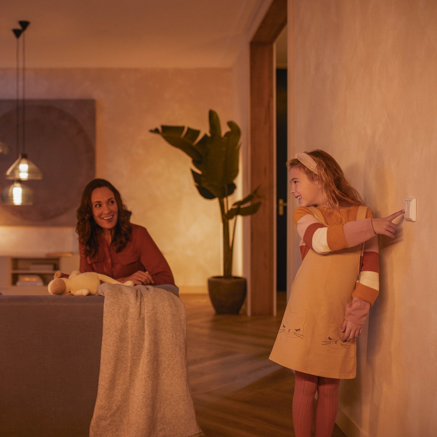 Philips Hue Vægafbrydermodul 2-pack monteret på væg, pige i lys kjole trykker på kontakt, kvinde ses i baggrunden.