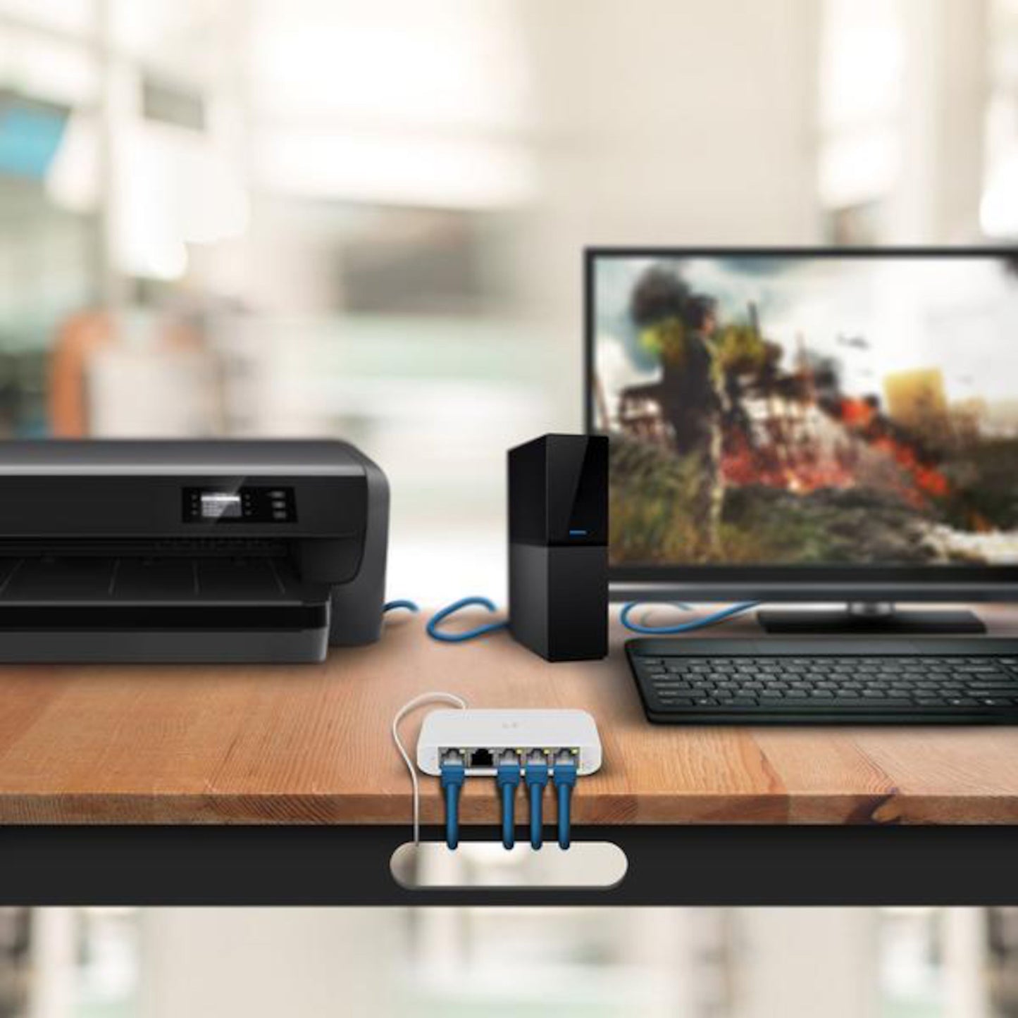 Ubiquiti Unifi USW Flex Mini Gigabit switch 5 porte, printer, desktop pc med skærm og tastatur med ethernetkabler på træbord.