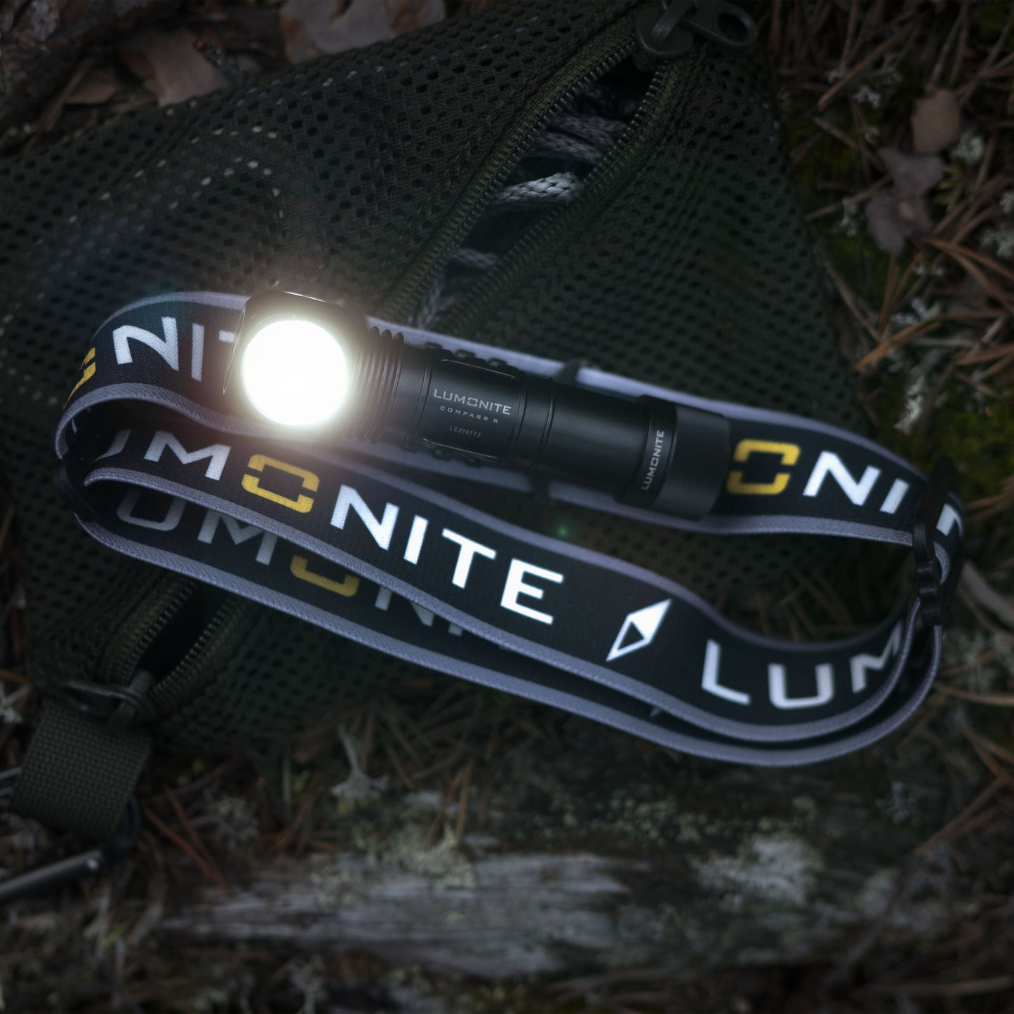 Lumonite Kompas sort pandelampe 1250 lm, IP69, synligt hvidt logo, på grøn netpose med blad og kviste.