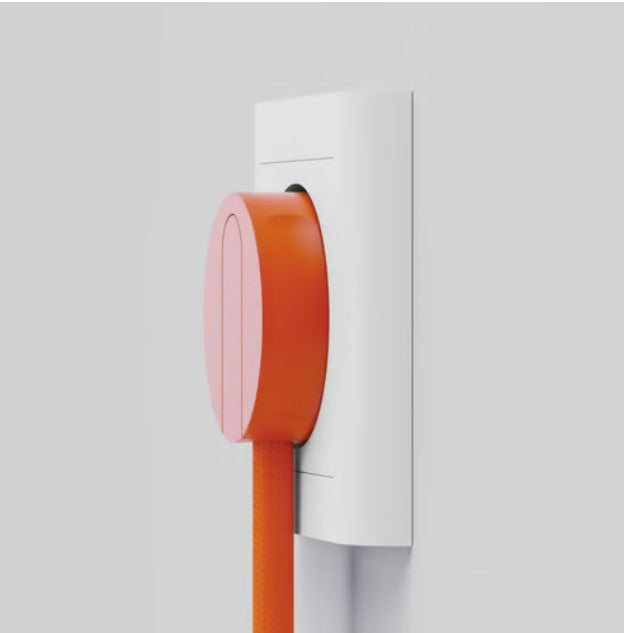 NORM K stikprop orange med jord, tilsluttet hvid stikkontakt, nærbillede med synlige stikben og farvedetaljer.
