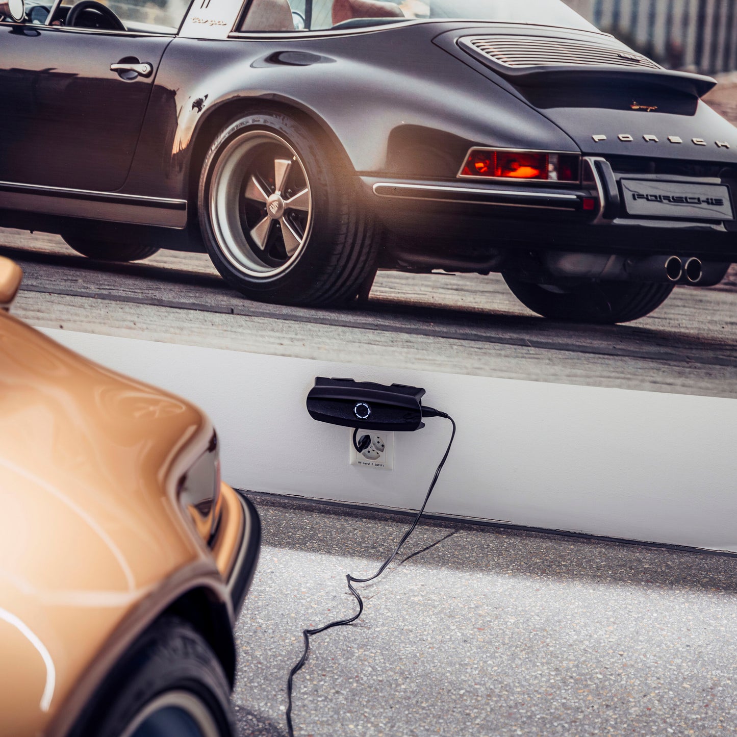 Ctek CS ONE Gen 2 smart batterioplader 12V vægmonteret, kabel i stikkontakt, sort Porsche-motiv, bagende af gul bil.