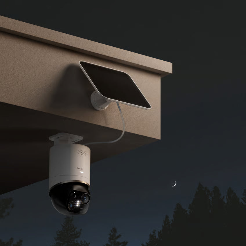 DREAME NAVO Elite 1 OutCam White 4K udendørskamera med solcellepanel monteret under tag – nat, træer og halvmåne i baggrunden.