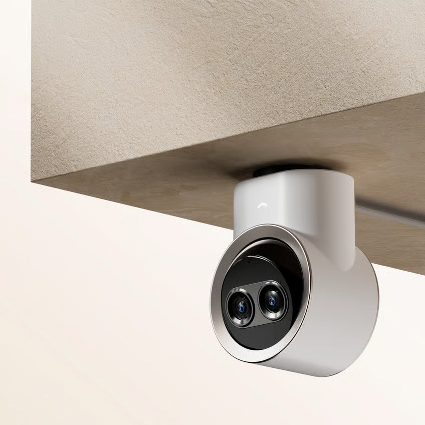 Dreame NAVO Elite 1 InCam indendørskamera med dobbeltlinse og AI-detektering, monteret under et beige loft, hvidt cylindrisk kabinet.