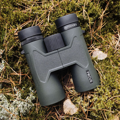 Focus Outdoor II 8x42 grøn kikkert ligger på moset underlag med tørre blade og grene.