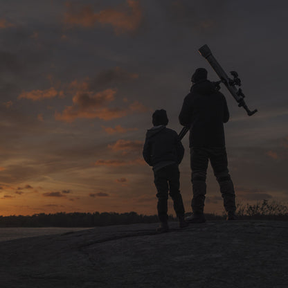 Celestron Powerseeker 60 AZ teleskop holdes af voksen ved siden af barn udendørs i solnedgang, teleskop tydeligt synligt.