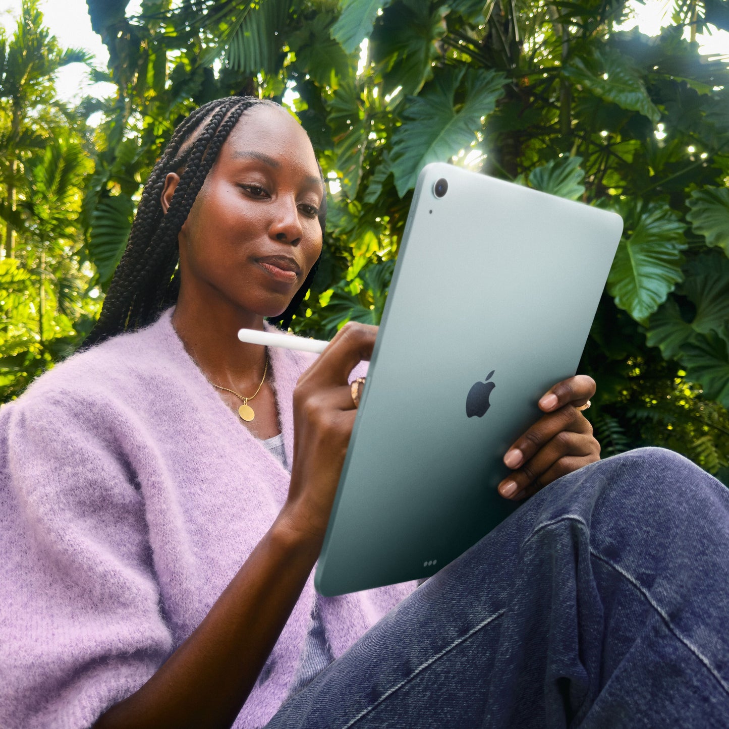 Apple iPad Air 11" (M4) 128GB Wifi lilla bruges med stylus udendørs, kvinde i lilla trøje, grøn baggrund.