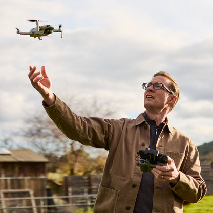 Drone i brug udendørs med 256 GB microSD Express, mand i briller og beige jakke opererer dronen nær træstruktur.