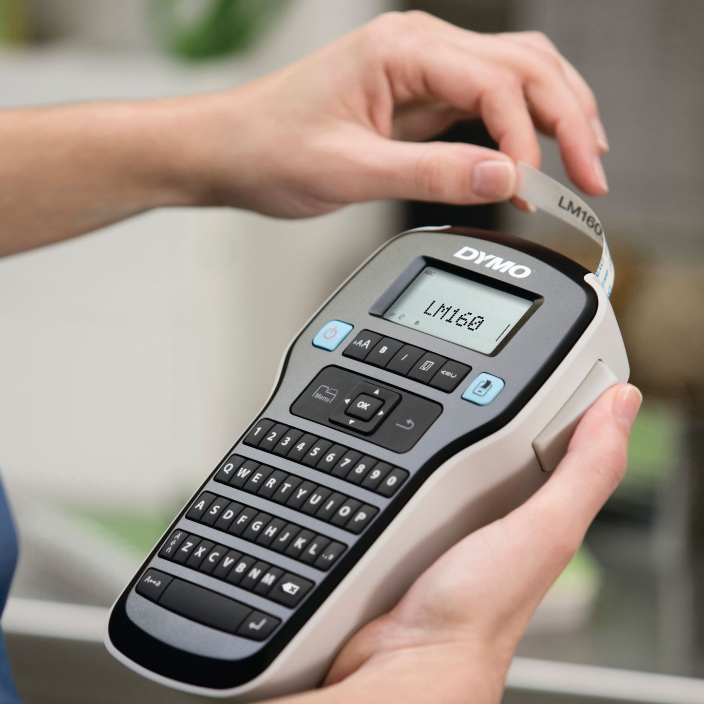 Dymo LabelManager 160 med QWERTY-tastatur og display, D1-label med teksten "LM160" trækkes ud af labelslot.