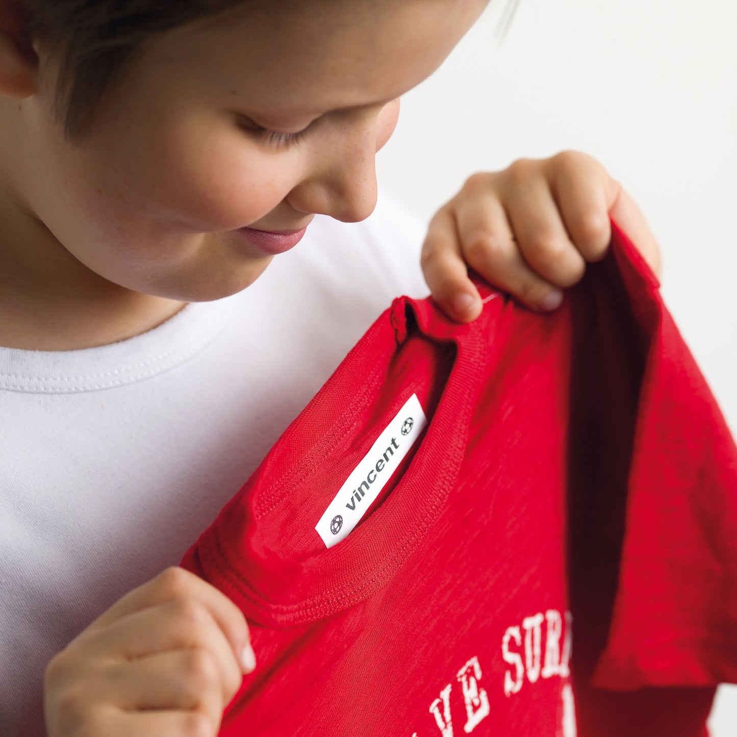 Rød T-shirt med Dymo Letratape Stofmærkningstape label i krav, navn Vincent trykt på mærket.