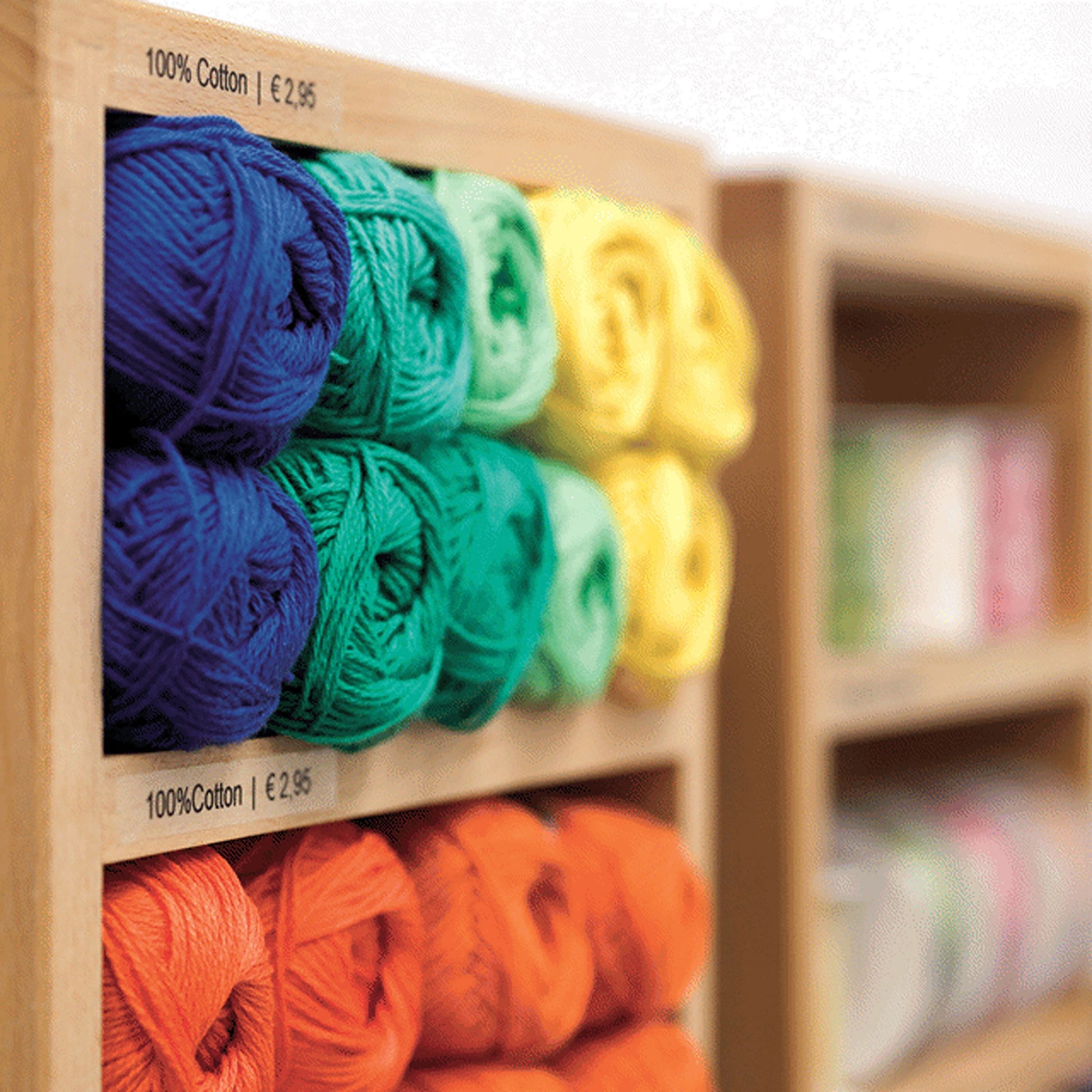 Hylder med garnnøgler i blå, grøn, gul og orange med mærkat "100 Cotton | €2,95" på D1-mærketape 12 mm klar.