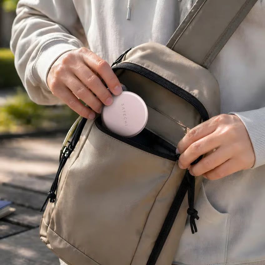 SATECHI OnTheGo 5-i-1 Neo-etui i farven „Rouge“ (lyserød) lægges i en beige crossbody-taske foran MacBook Neo og USB-C-hubben.