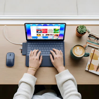 Satechi USB-C Snap Hub Neo Indigo til MacBook Neo ses på et træbord sammen med en trådløs mus, en notesbog, en pen og et par briller.