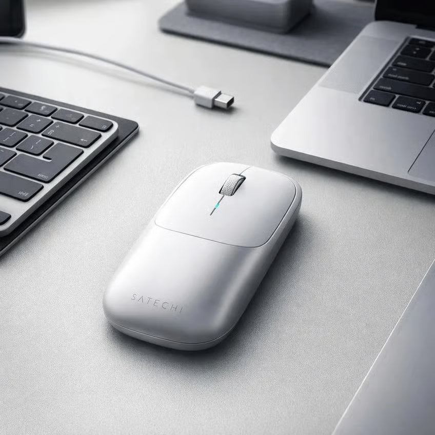 SATECHI Slim X i sølv med Bluetooth 5.3 ved siden af en bærbar computer, et tastatur og et USB-C-kabel på et gråt bord.