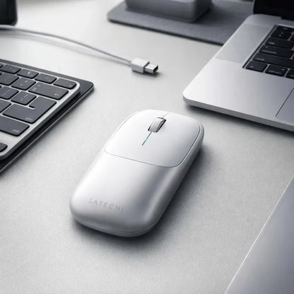 SATECHI Slim X i sølv med Bluetooth 5.3 ved siden af en bærbar computer, et tastatur og et USB-C-kabel på et gråt bord.