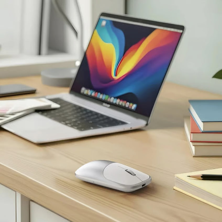 Satechi Slim EX Mus, sølvfarvet ved siden af en sølvfarvet bærbar computer med farverig skærm og USB-C på et skrivebord af træ.