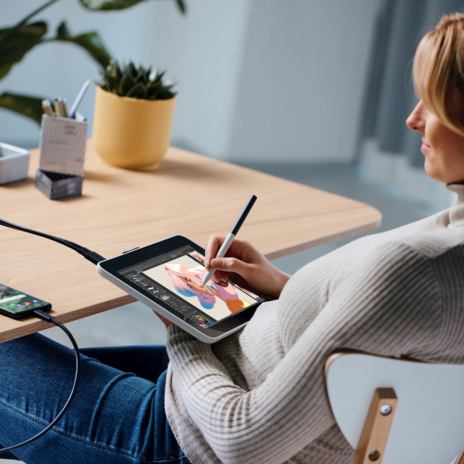 Wacom En 12-tommers bærbar computer til digital kunst, synligt forbundet til smartphone på skrivebord med tegnetilbehør.