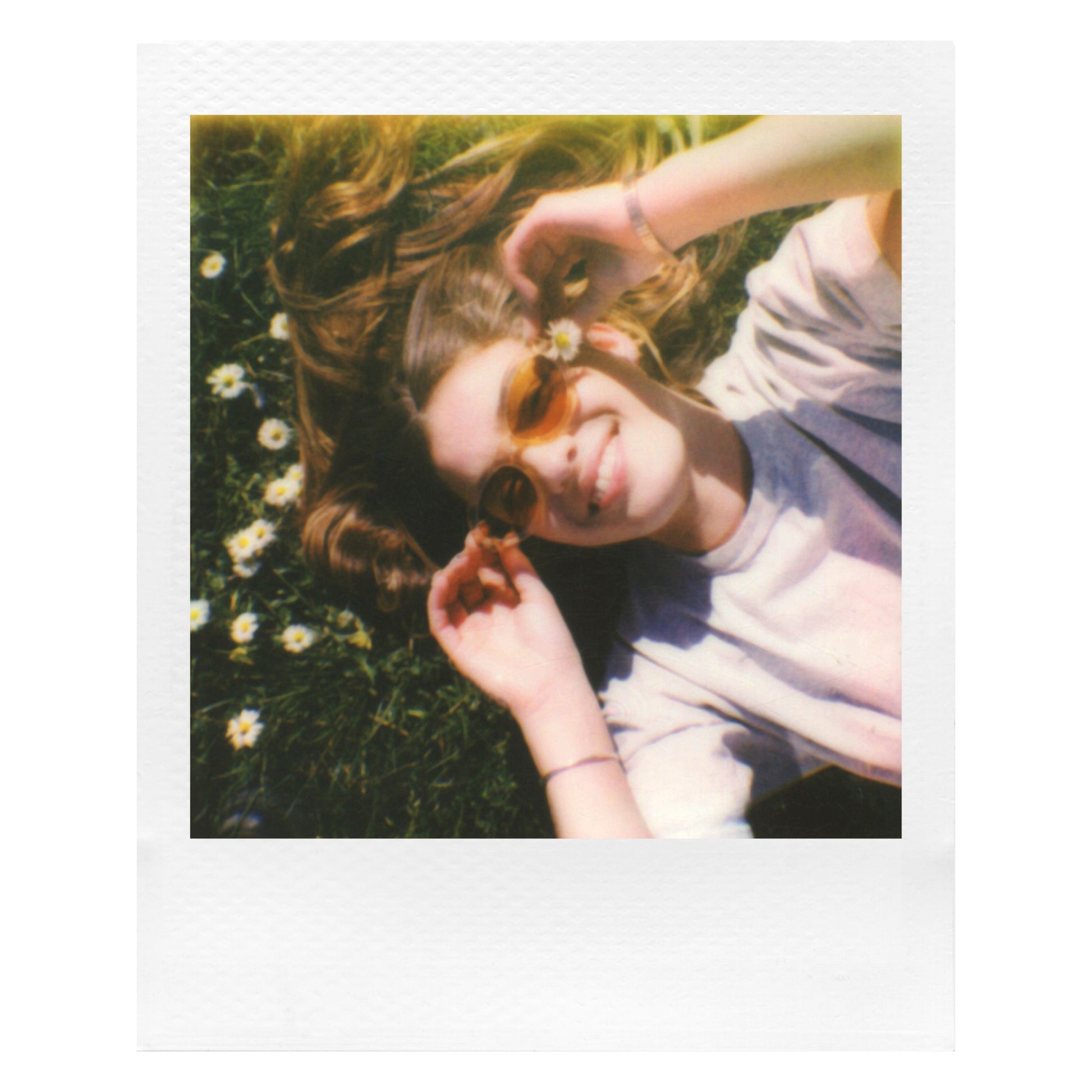Polaroid Go Film Dobbelt Pakke 16 billeder bruges til instant foto af ung med langt hår på græs omgivet af små hvide blomster.