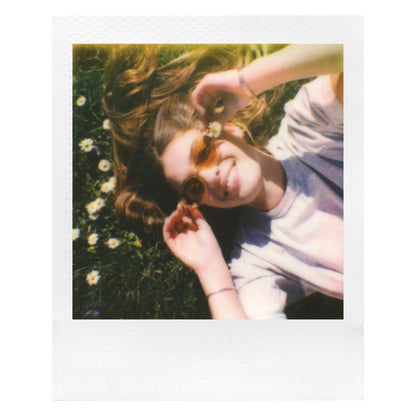 Polaroid Go Film Dobbelt Pakke 16 billeder bruges til instant foto af ung med langt hår på græs omgivet af små hvide blomster.