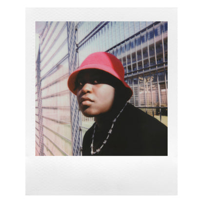 Person med rød bøllehat, sorte tøj og kæde fotograferet ved metalhegn på Polaroid Go Film Dobbelt Pakke 16 billeder.