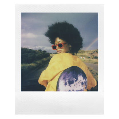 Polaroid Go Film Dobbelt Pakke 16 billeder, portræt med stor afro, røde solbriller, gul jakke med måne på ryggen.