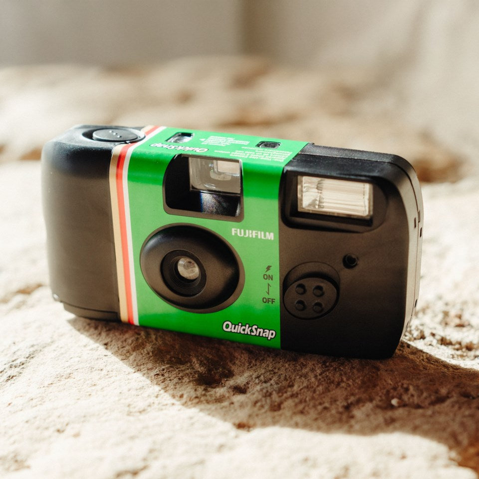 Fujifilm QuickSnap Flash engangskamera grøn/sort, 27 billeder, ligger på lyst tekstureret underlag.