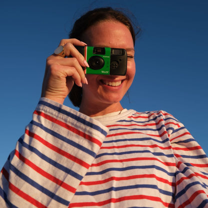 Fujifilm QuickSnap Flash Engangskamera 27 billeder ses i brug, holdes op til øjet af kvinde i stribet skjorte.