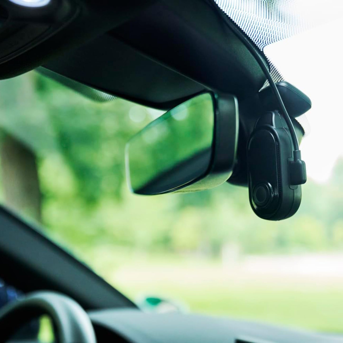 Nextbase Piqo 1K dashcam monteret ved bakspejl på forrude i bil, natur sløret baggrund, modelnavn synligt.