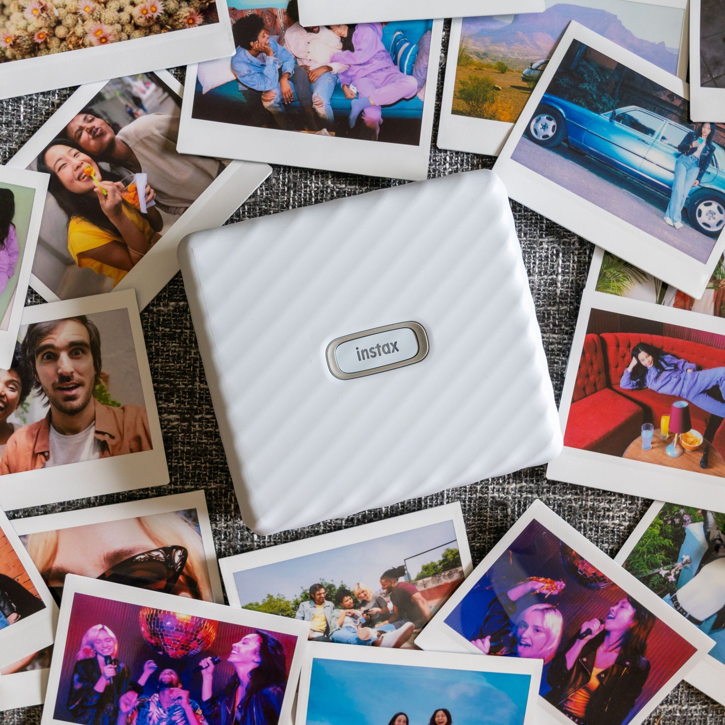 Fujifilm Instax Link Wide Hvid printer omgivet af farverige Instax Wide-fotos af personer, landskaber og begivenheder.
