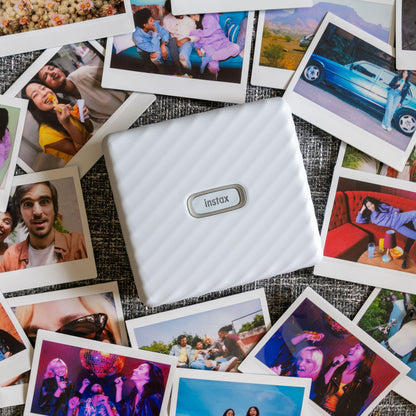 Fujifilm Instax Link Wide Hvid printer omgivet af farverige Instax Wide-fotos af personer, landskaber og begivenheder.