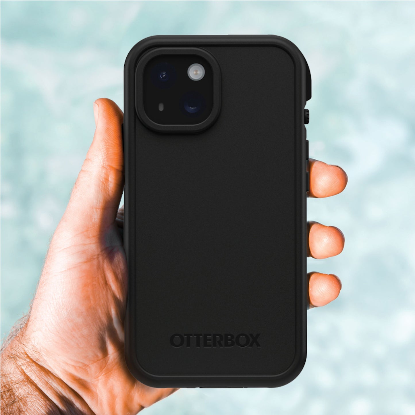 IPhone 15 i sort Otterbox Fre mobilcover, MagSafe-kompatibel, håndholdt med sløret lyseblå baggrund.