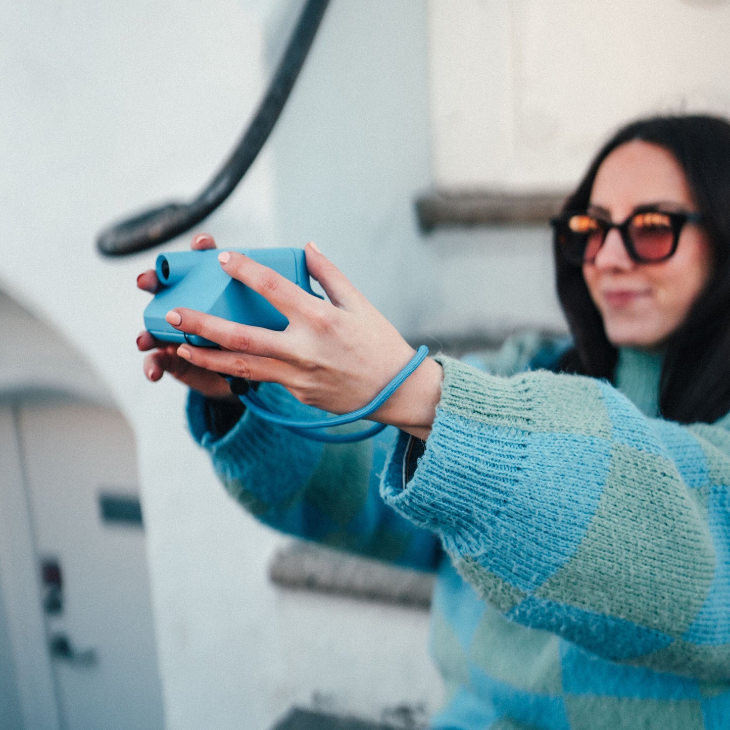 Polaroid Go Gen2 instant kamera bæres af kvinde i blågrøn sweater og solbriller, udendørs ved trappe.