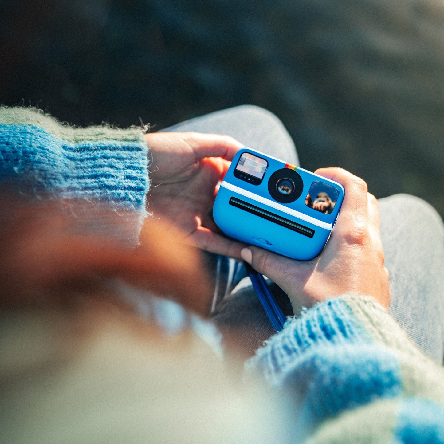 Polaroid Go Gen2 instant kamera med regnbuestribe og film slot holdes af hænder i blå striktrøje.