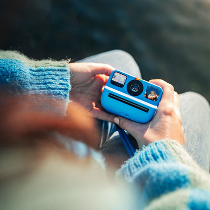 Polaroid Go Gen2 instant kamera med regnbuestribe og film slot holdes af hænder i blå striktrøje.