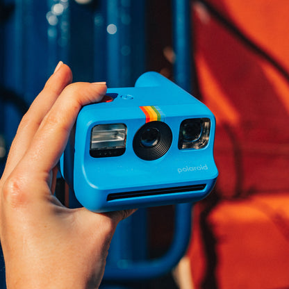 Polaroid Go Gen2 instant kamera i blå med regnbuestribe, linse og blitz ses forfra i hånd.