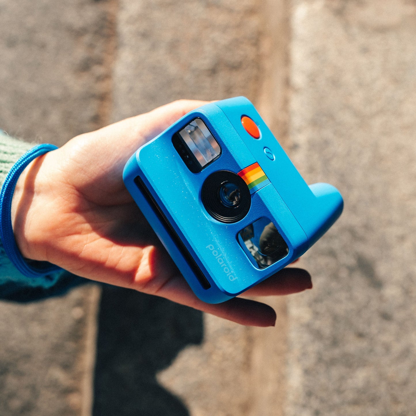 Polaroid Go Gen2 Instant kamera, blå, holdes i hånd udendørs med sollys på kamera og hånd.