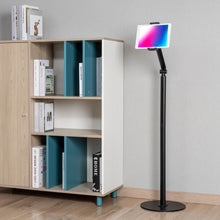 Stabilt gulvstativ til tablet 4,7-12,9" i metal ved siden af hvid-træ reol med bøger og skulptur, lyst trægulv.