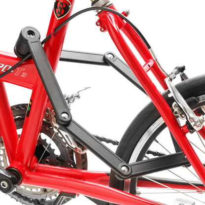 Luxorparts foldbart cykellås med nøgle monteret ved stel, tæt på sort baghjulsophæng, bremse og gear på rød cykel.