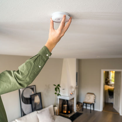 Housegard Pebble røgalarm monteres i loft i stue, person med grøn trøje, pejs synlig i baggrund.