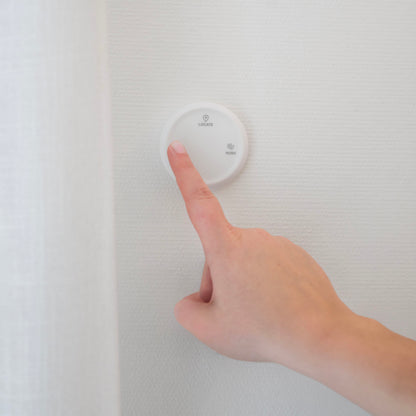 Housegard Luma trådløs fjernbetjening, rund og hvid, monteret på væg, med LOCATE og HEALTH knapper.