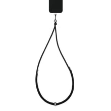 IDEAL OF SWEDEN Cord Phone Strap, justerbar mobilrem med metalldetaljer monteret på sort smartphone.