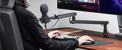 Deltaco lavprofil mikrofonarm sort holder mikrofon ved skrivebord med tastatur, mus og to store skærme med digitalt indhold.