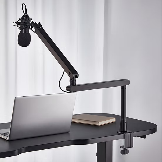 Deltaco lavprofil mikrofonarm sort med monteret mikrofon på justerbar arm, laptop og lukket notesbog på mørkt skrivebord.