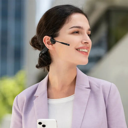 Shokz OpenComm2 trådløse hovedtelefoner med støjreducerende mikrofoner bæres af kvinde, lavendel blazer, smartphone.