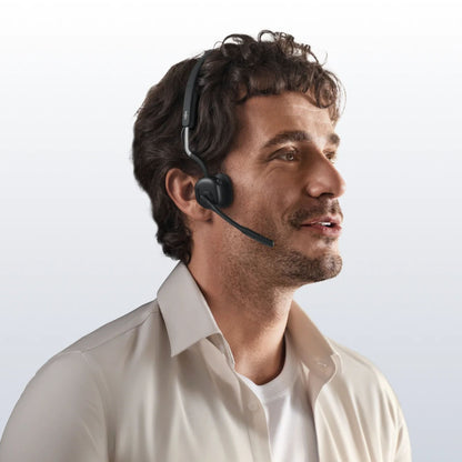 Shokz OpenMeet kontorhovedtelefoner med åbent øre-design, trådløs, mikrofon, bæres af mand med krøllet hår og beige skjorte.