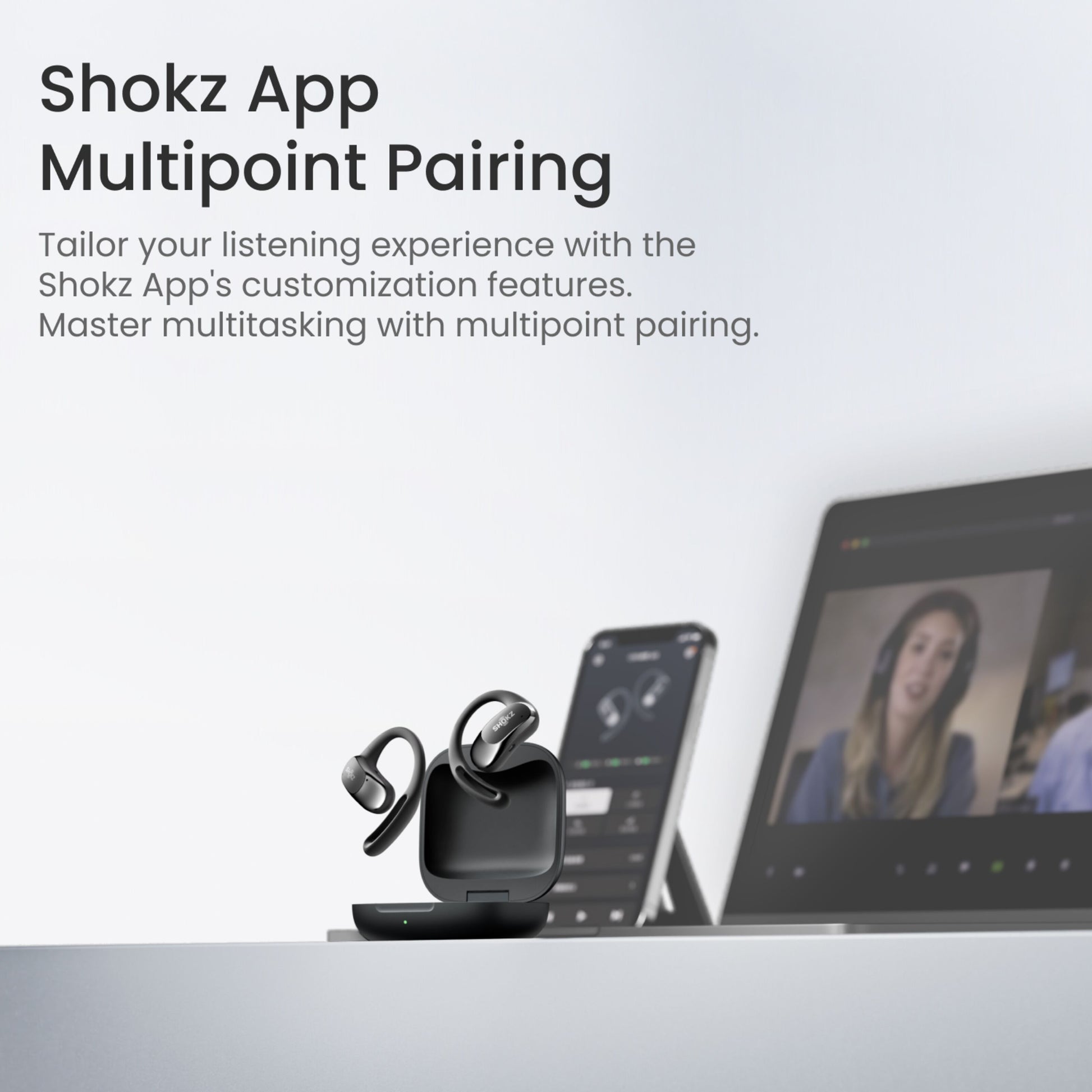 Shokz OpenFit Air trådløse øretelefoner sorterer i etui ved laptop med videomøde og smartphone med Shokz app.