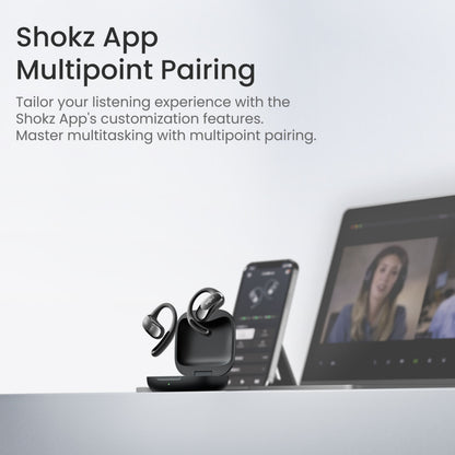 Shokz OpenFit Air trådløse øretelefoner sorterer i etui ved laptop med videomøde og smartphone med Shokz app.