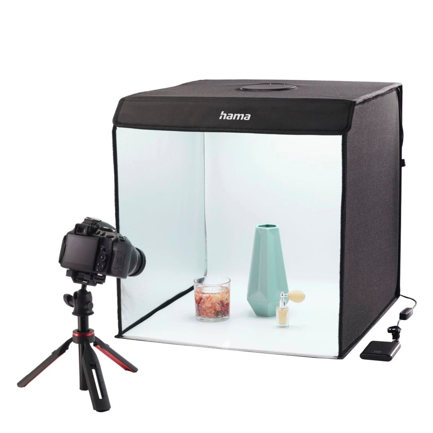 Hama Mini-fotostudie ToGo med LED-ringlys, sort med halvgennemsigtig front, viser oplyst turkis vase, duftlys og parfume.