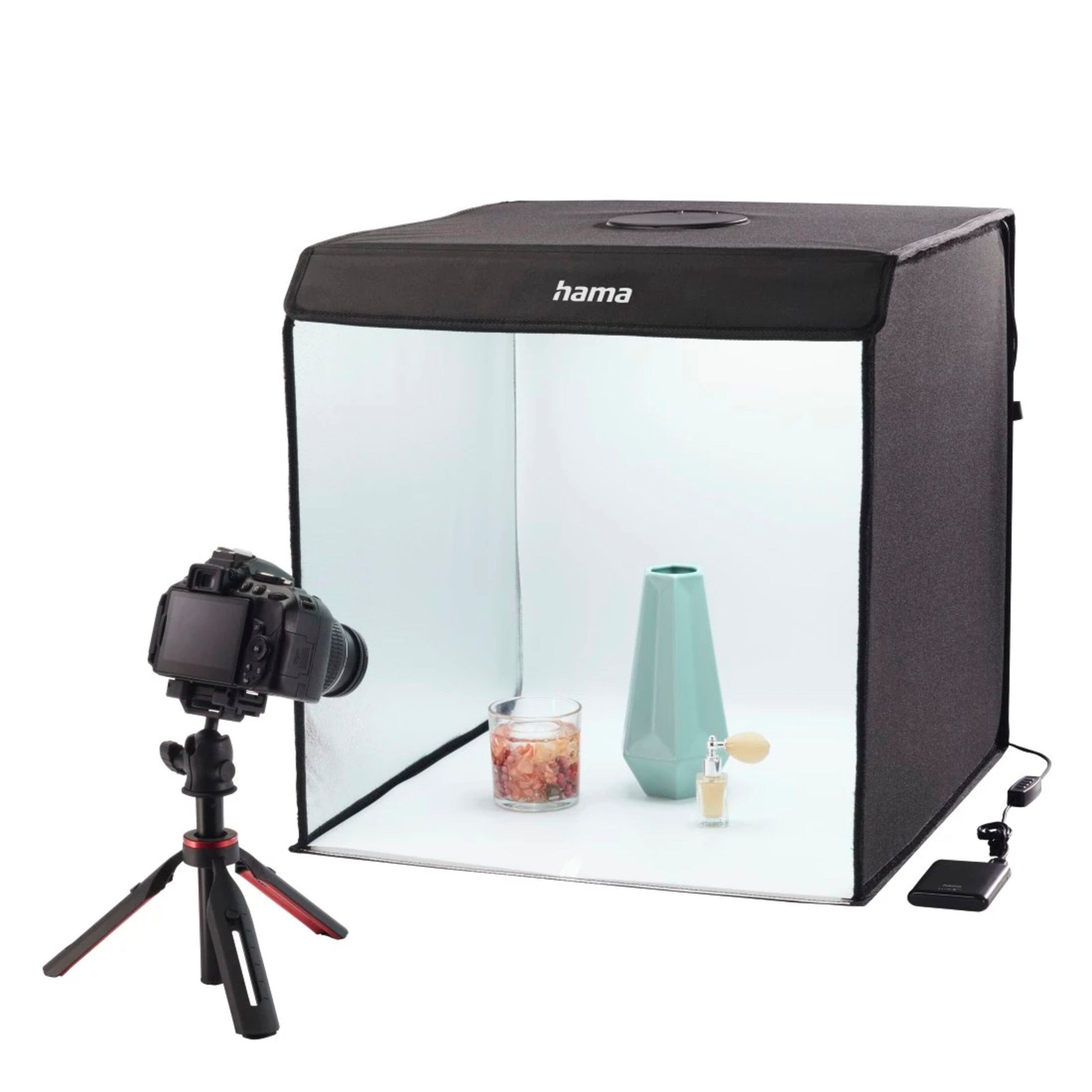 Hama Mini-fotostudie ToGo med LED-ringlys, sort med halvgennemsigtig front, viser oplyst turkis vase, duftlys og parfume.